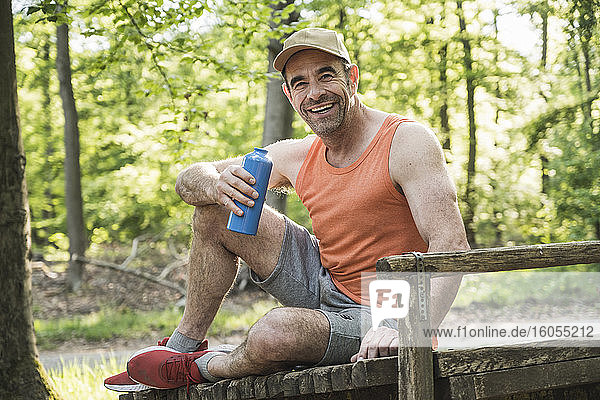 Glücklicher reifer Mann sitzt mit Wasserflasche im Park