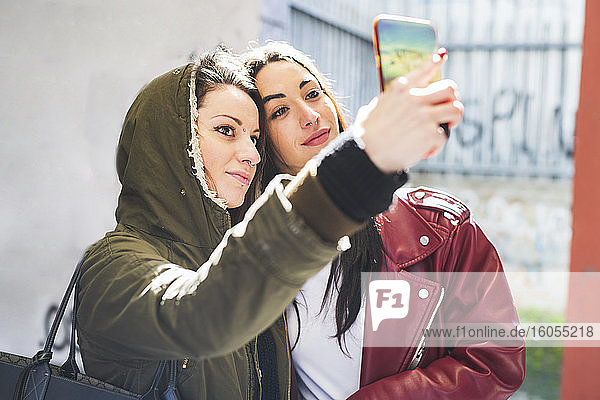 Frau  die ein Selfie mit ihrer Freundin macht  während sie in der Stadt an der Wand steht