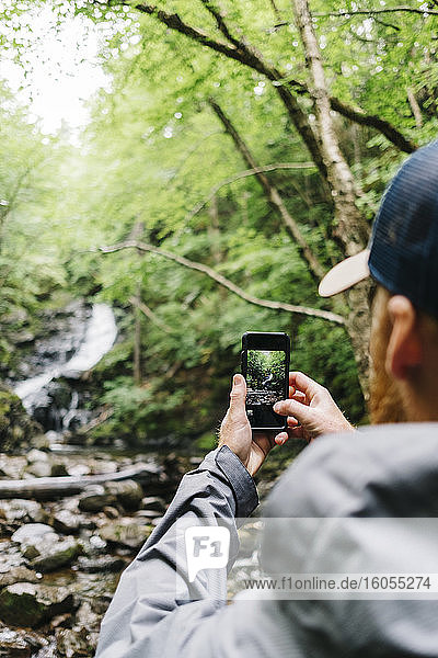 Man photographing waterfall while hiking in forest