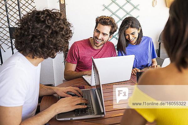 Lächelnde junge Freunde benutzen Laptops  während sie am Tisch im Hinterhof sitzen