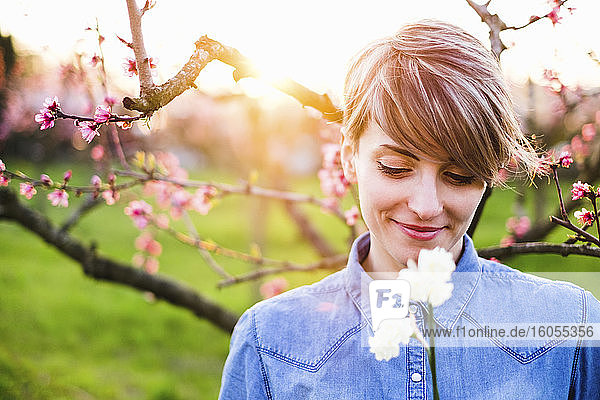 Nahaufnahme einer lächelnden Frau  die bei Sonnenuntergang Blumen im Park betrachtet