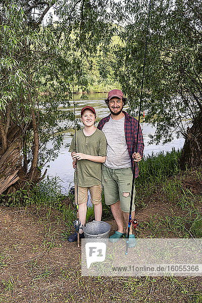 Glücklicher Vater und Sohn mit Angelrute am Flussufer stehend