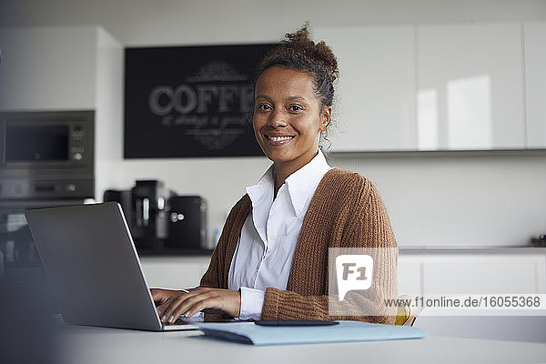Porträt einer lächelnden Geschäftsfrau  die in der Küche am Laptop arbeitet