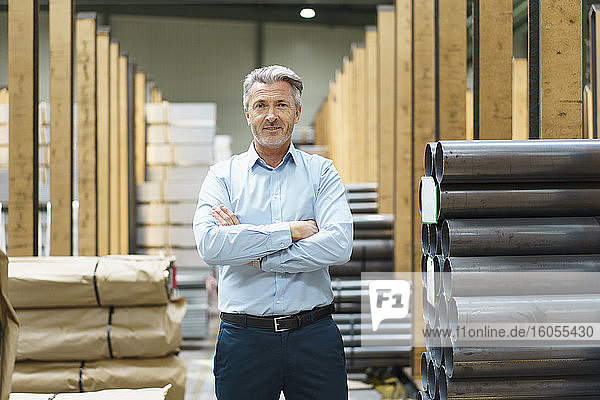 Portrait of a confident mature businessman in a factory storehouse with steel pipes