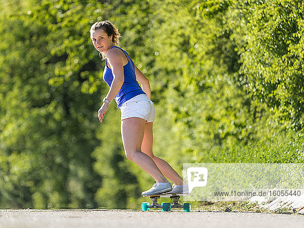 Junge Frau Skateboarding auf der Straße von Pflanzen während sonnigen Tag