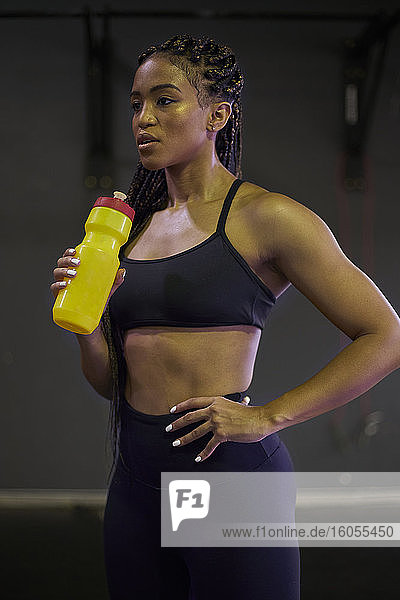 Nachdenkliche Sportlerin  die eine Wasserflasche hält  während sie im Fitnessstudio steht