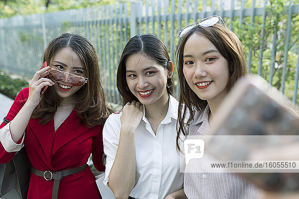 Smiling woman taking selfie with friends while standing in park