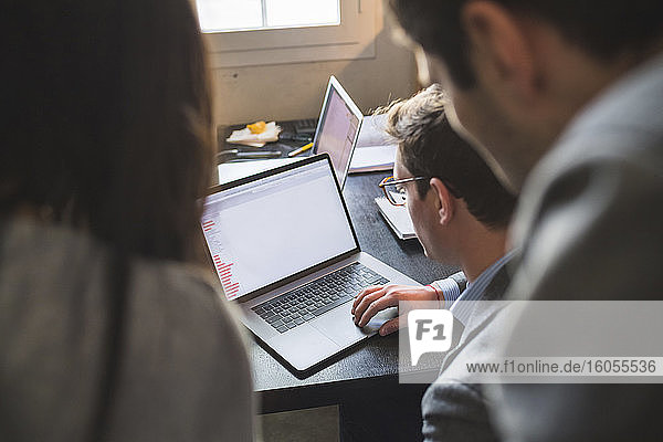 Drei Geschäftsleute teilen sich einen Laptop am Schreibtisch im Büro