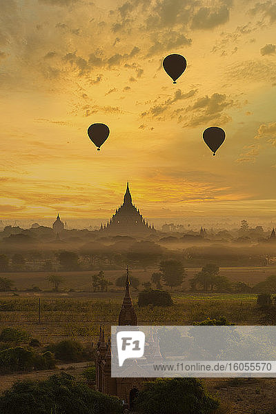 Myanmar  Mandalay Region  Bagan  Silhouettes of hot air balloons flying over ancient temples at foggy dawn