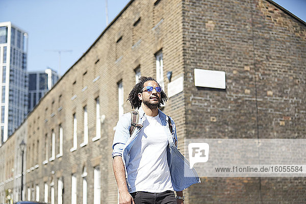 Portrait of young man with backpack and sunglasses walking on residential street  London  UK