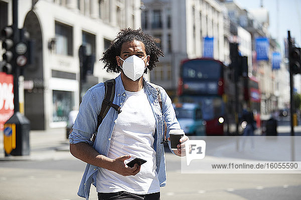 Portrait of young man wearing protective mask crossing the street  London  UK