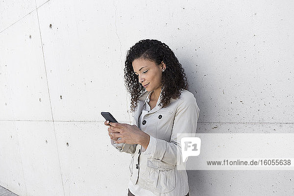 Stilvolle Geschäftsfrau  die ein Smartphone benutzt  während sie an der Wand steht