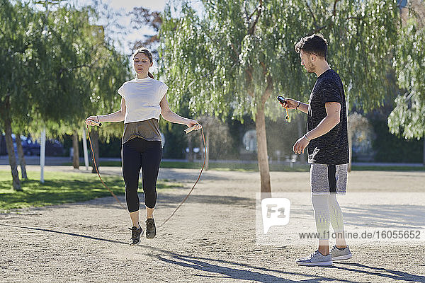 Frau beim Training mit Trainer  der im Park Seil springt