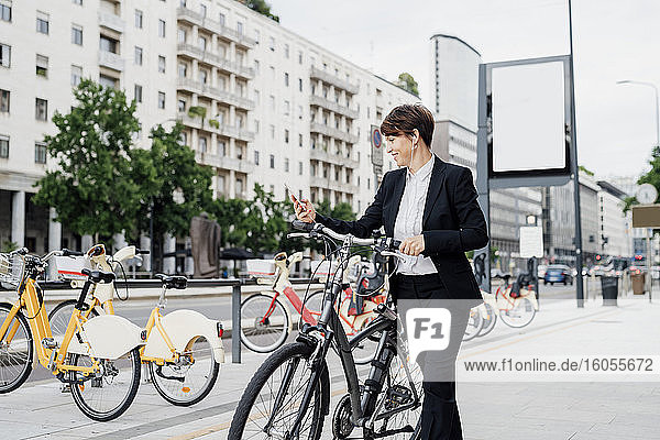 Geschäftsfrau hört Musik  während sie mit dem Fahrrad auf dem Gehweg in der Stadt spazieren geht