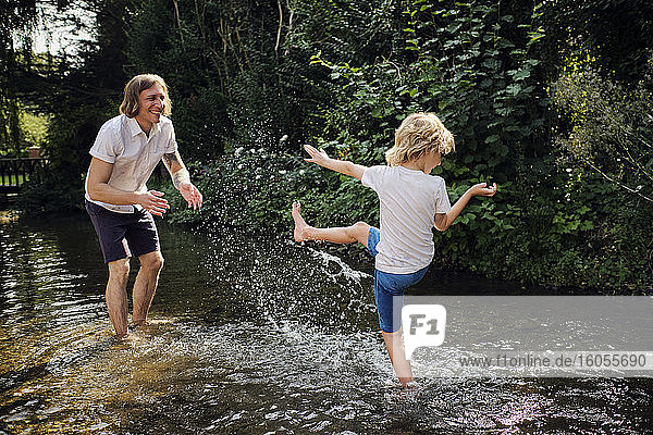 Father and son playing in stream during sunny day at forest