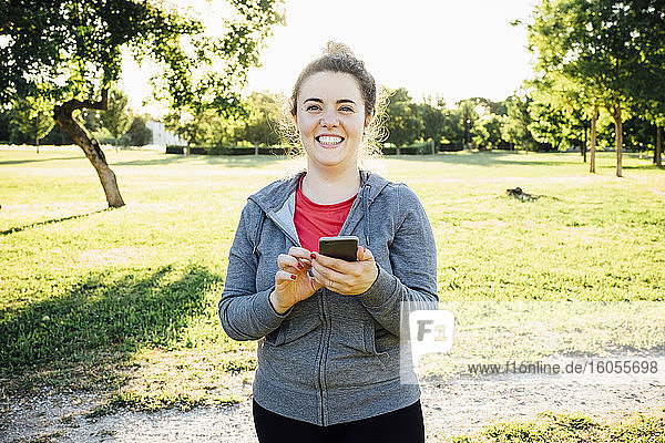 Lächelnde Joggerin mit Smartphone im Park
