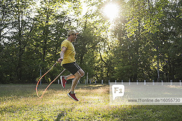 Glücklicher reifer Mann  der mit einem Springseil auf einer Wiese im Park trainiert