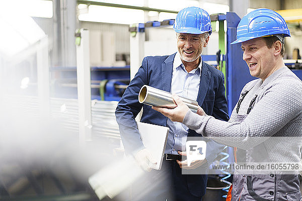 Businessman and worker in a factory holding steel pipe