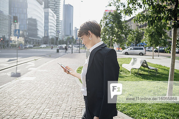 Weibliche Fachkraft  die ein Mobiltelefon benutzt  während sie auf dem Bürgersteig in der Stadt steht