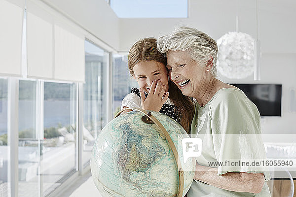 Lachende Großmutter und Enkelin mit Globus in einer Villa