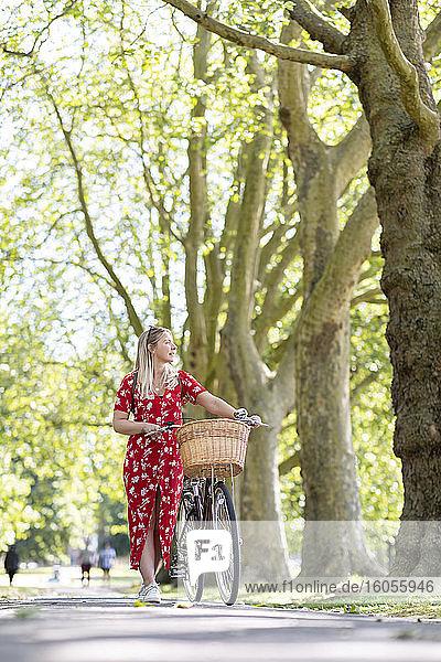 Frau schaut weg  während sie mit dem Fahrrad auf dem Gehweg in einem öffentlichen Park spazieren geht