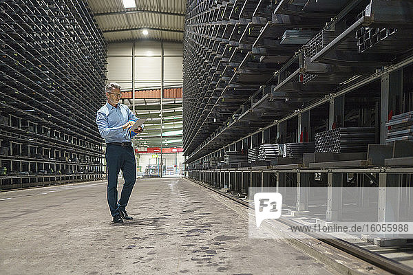 Mature businessman using tablet in a high rack warehouse of a factory
