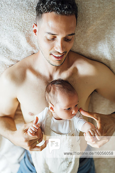 Cute baby boy lying on shirtless father at home
