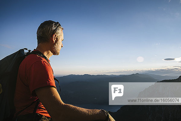 Älterer Mann mit Rucksack  der bei Sonnenuntergang die Berge gegen den Himmel betrachtet  Orobie  Lecco  Italien