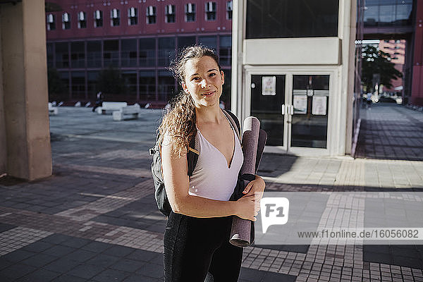 Sportliche junge Frau hält eine Gymnastikmatte  während sie auf der Straße steht