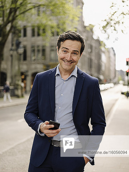 Porträt eines glücklichen reifen Geschäftsmannes mit Smartphone in der Stadt