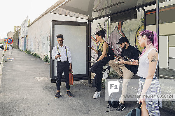 Gruppe von Freunden mit Smartphones an einer Bushaltestelle in der Stadt