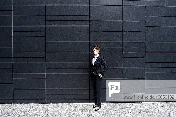 Selbstbewusste Geschäftsfrau steht auf dem Bürgersteig vor einem modernen Gebäude in der Stadt