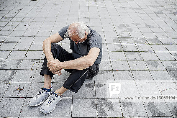 Müder älterer Mann sitzt auf dem Fußweg in der Stadt