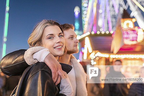 Smiling woman with boyfriend standing in amusement park at night