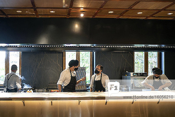 Köche mit Gesichtsschutzmasken arbeiten gemeinsam in einer Restaurantküche