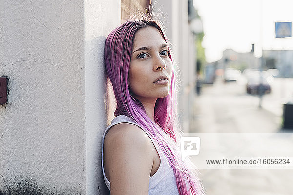 Portrait of a stylish young woman with pink hair leaning against a wall in the city