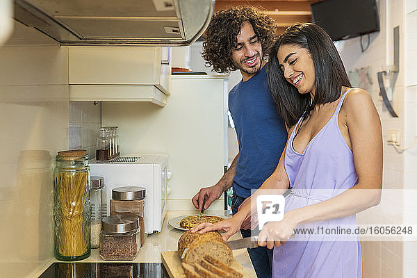 Smiling young couple preparing meal in kitchen at home