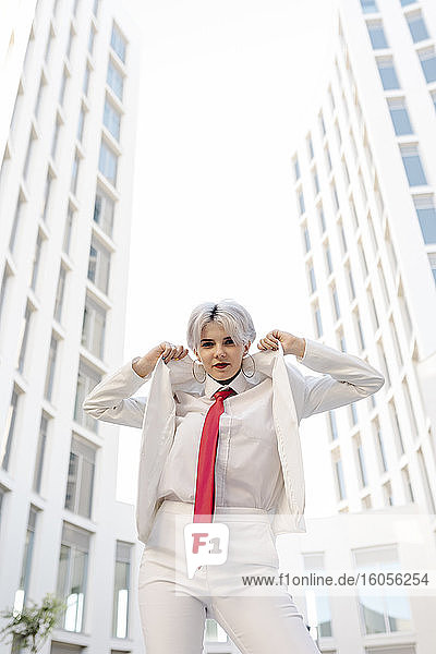 Coole junge Frau im weißen Anzug  die vor einem Gebäude in der Stadt steht