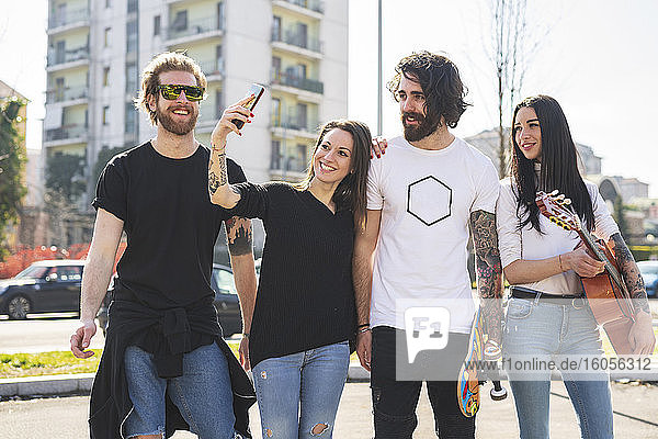 Smiling woman taking selfie with friends while standing in city