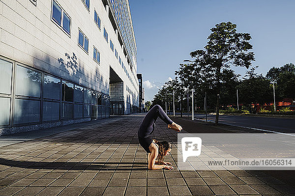 Junge Frau beim Yoga auf dem Bürgersteig in der Stadt an einem sonnigen Tag