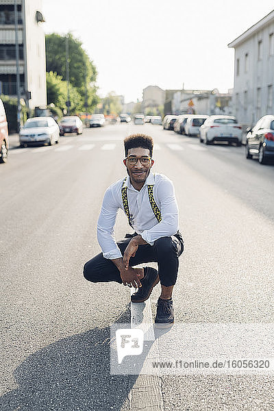 Porträt eines selbstbewussten stilvollen jungen Mannes  der auf der Straße in der Stadt hockt