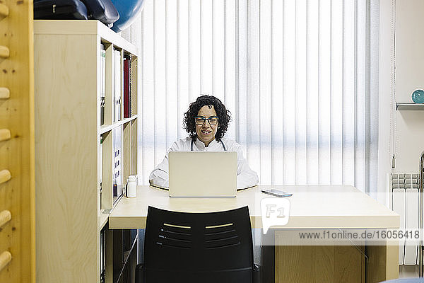 Weiblicher Arzt  der einen Laptop benutzt  während er an einem Schreibtisch in einem Büro einer medizinischen Klinik sitzt