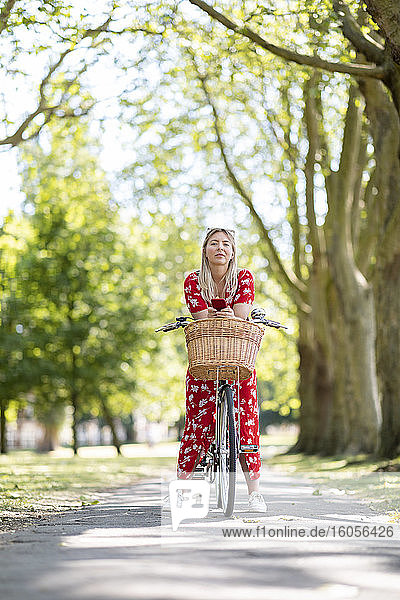Frau hält Smartphone  während sie sich in einem öffentlichen Park auf ein Fahrrad stützt