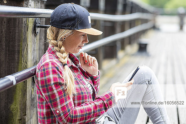 Woman with braided hair using smart phone while sitting on bridge