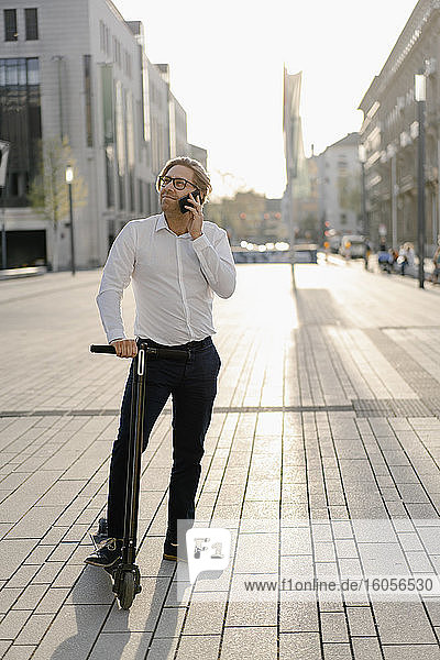 Geschäftsmann mit Kick-Scooter am Telefon in der Stadt