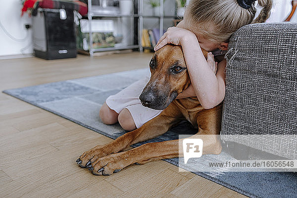 Girl embracing dog while relaxing on carpet in living room at home