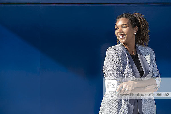 Lächelnde Geschäftsfrau vor einer blauen Wand