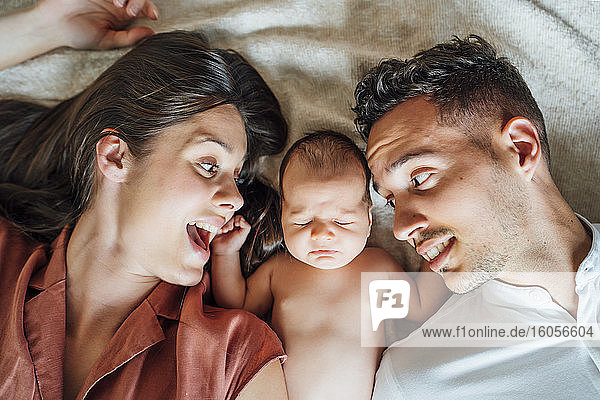 Cheerful parents lying with baby boy on bed at home