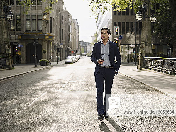 Mature businessman walking on a city street holding smartphone