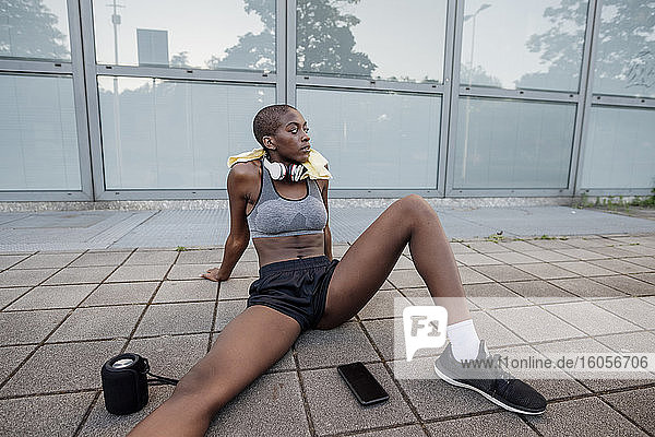 Müde Sportlerin mit rasiertem Kopf auf dem Fußweg in der Stadt sitzend